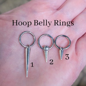 May include: Three silver belly button rings with pointed ends. The rings are numbered 1, 2, and 3.