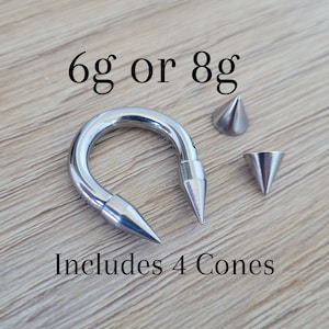 May include: A silver horseshoe-shaped piercing with two pointed ends and four silver cone-shaped ends. The text "6g or 8g" and "Includes 4 Cones" is visible in the image.