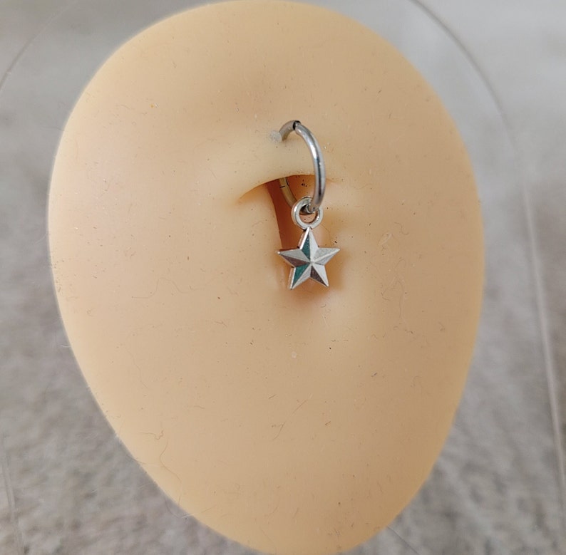 May include: A silver star charm dangling from a silver hoop piercing