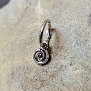 May include: A silver hoop earring with a spiral charm. The earring is made of metal and has a simple design.