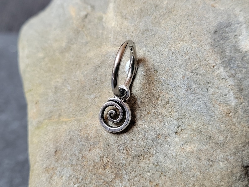 May include: A silver hoop earring with a spiral charm. The earring is made of metal and has a simple design.