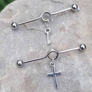 May include: Two silver industrial barbell earrings with charms. One charm is a silver key and the other is a silver cross.