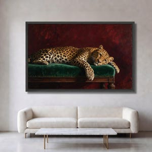 May include: A framed rectangular wall art print featuring a leopard with gold and black spotted fur resting on a dark green velvet bench. The bench has wooden legs and brass nailhead trim. The background is a deep, textured dark red color.