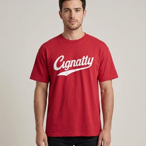 Könnte beinhalten: Ein rotes T-Shirt mit Rundhalsausschnitt und dem weißen Schriftzug "Cignatty" in Schreibschrift. Das Model trägt eine schwarze Jeans. Das Shirt ist aus einem weichen Material.