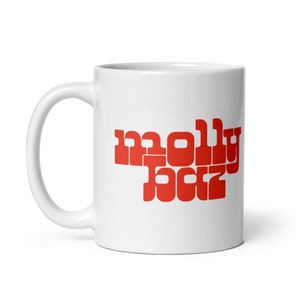 Op de afbeelding: Witte keramische mok met een rode "molly boz" opdruk. De mok heeft een gebogen oor en een glanzende afwerking. De tekst is in een vet, retro lettertype.