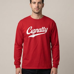 Könnte beinhalten: Ein rotes Langarmshirt mit dem weißen Schriftzug "Cignatty" auf der Brust. Das Shirt hat einen Rundhalsausschnitt und ist aus einem weichen Material. Das Model trägt eine schwarze Jeans.