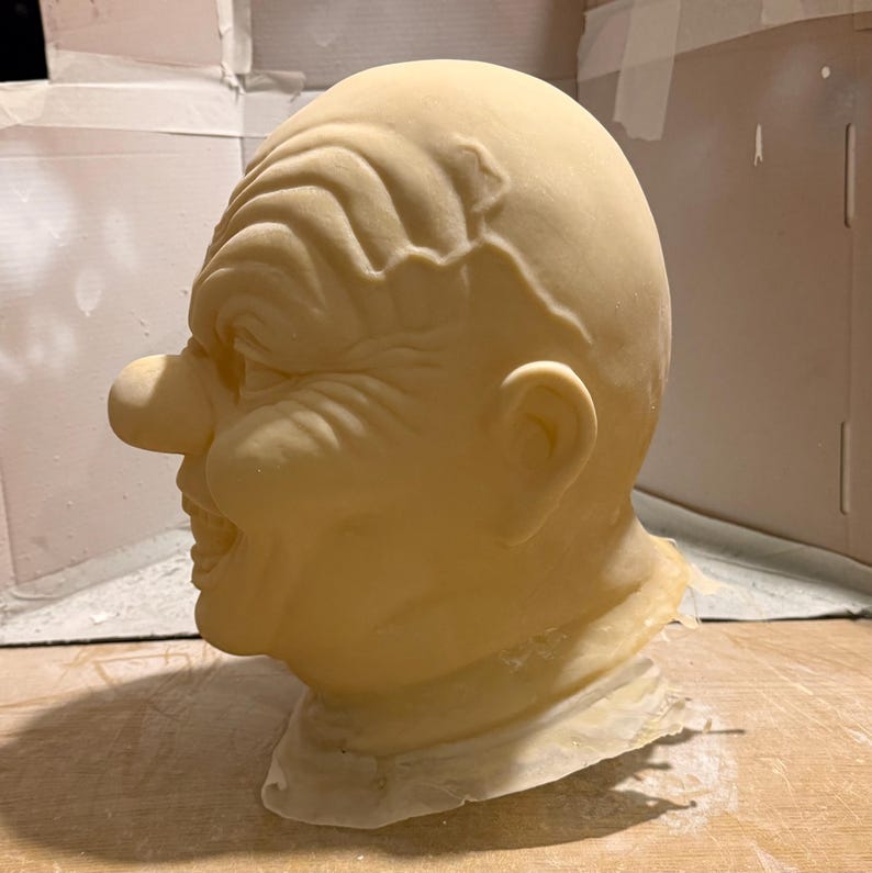 Peut inclure: Un masque p&acirc;le en forme de clown avec des traits exag&eacute;r&eacute;s. Le masque a un grand nez, un large sourire &eacute;dent&eacute; et des rides profondes sur le front et les joues. Le masque est fait d'un mat&eacute;riau de couleur claire et est probablement destin&eacute; &agrave; un costume ou &agrave; un usage th&eacute;&acirc;tral.