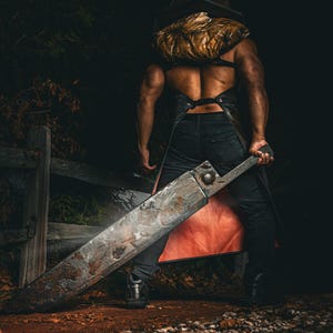 Könnte beinhalten: Ein Kostüm bestehend aus einer großen, verwitterten, metallisch wirkenden Pyramiden-Kopfbedeckung, einer dunkelbraunen, lederartigen Schürze mit metallischem Glanz und einer massiven, rostigen, rechteckigen Klinge, getragen über dunkler Hose und Stiefeln.