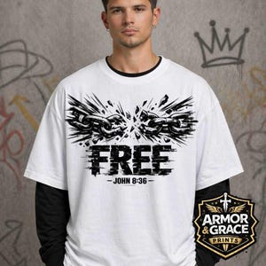 May include: White t-shirt with a black graphic of a broken chain and the word "FREE" in bold letters. The text "JOHN 8:36" is below the word "FREE". The shirt has a black long-sleeve undershirt.