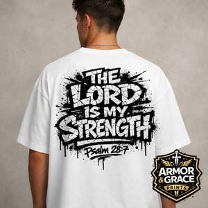 Peut inclure: T-shirt blanc avec l'inscription "THE LORD IS MY STRENGTH" en noir, avec un effet vieilli. Le texte "Psalm 28:7" est en dessous. Un logo est également présent en bas à droite.