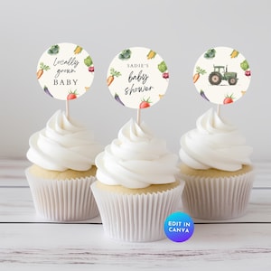 Op de afbeelding: Drie cupcakes met witte frosting en decoratieve toppers. De toppers bevatten tekst en illustraties van groenten en een groene tractor. Eén zegt "Locally grown BABY", een andere "Sadie's baby shower".