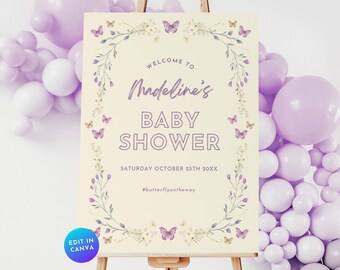 May include: A welcome sign for a baby shower with a floral wreath and butterflies. The sign is cream colored with purple butterflies and green leaves. The text reads "Welcome to Madeline's Baby Shower, Saturday October 25th 20XX, #butterflyontheway".