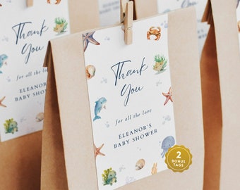 May include: Thank you favor bags with a blue and white ocean-themed design. The bags feature a dolphin, starfish, seashells, and the text "Thank You for all the love Eleanor's Baby Shower".