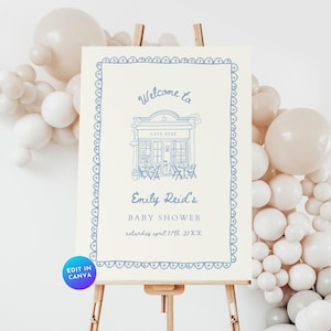 May include: A baby shower welcome sign on an easel. The sign has a light cream background with a blue border and text. The text reads "Welcome to Cafe Bebe, Emily Reid's Baby Shower, Saturday April 17th 20XX".