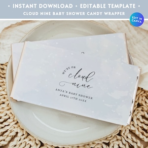 May include: A blue and white baby shower candy wrapper with a white background and a black design. The design says "We're on cloud nine" with the words "Anya's Baby Shower" and "April 17th 20XX" below. The design is surrounded by small white stars.