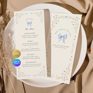 Może przedstawiać: Jasnoniebieskie i białe menu na baby shower z kwiatową ramką i niebieską kokardką. Menu zawiera przystawki, danie główne, deser i napoje. Tekst "Let's Eat" znajduje się na górze menu. Tekst "Sweet Bows & Tiny Toes" znajduje się na górze prawej strony menu. Tekst "Charlotte's Baby Shower" znajduje się na dole prawej strony menu.