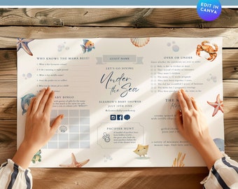 Puede incluir: Un mantel individual imprimible para una baby shower con temática oceánica, en azul y blanco. El mantel individual incluye juegos como "¿Quién conoce mejor a la mamá?" y "Más o menos", así como un menú para la ducha. El mantel individual tiene un diseño de acuarela con conchas marinas, estrellas de mar y un cangrejo.