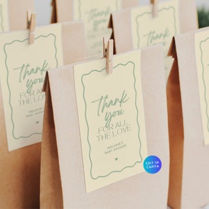 May include: Brown paper gift bags with cream-colored tags. The tags have a green wavy border and the words "Thank you for all the love" in green script. A small wooden clip holds each tag.