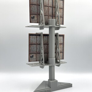 May include: A gray 3D-printed model of a double-stacked billboard structure with a central support pole and triangular base. The billboards feature a brown, grid-patterned surface with the text "elf @greeblerelf" and the base reads "GreeblerElf 2025".