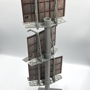 May include: A three-tiered gray plastic model billboard structure featuring a central vertical pole and a triangular base. Each level holds a rectangular sign with a weathered, rusted metal texture and the printed text elf @greethkrell.