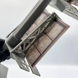May include: A miniature gray plastic billboard structure featuring a rectangular display panel with a printed brown wood-grain pattern and black border lines. The model includes a central support pole and a detailed truss framework supporting the sign.