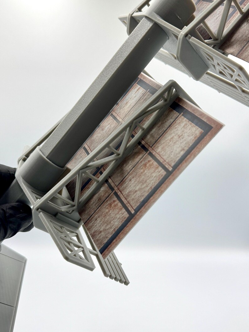 May include: A miniature gray plastic billboard structure featuring a rectangular display panel with a printed brown wood-grain pattern and black border lines. The model includes a central support pole and a detailed truss framework supporting the sign.