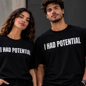 Op de afbeelding: Een zwart T-shirt met korte mouwen en een ronde hals, voorzien van de witte tekst I HAD POTENTIAL in een vet, schreefloos lettertype op de borst. Het kledingstuk is gemaakt van effen zwarte stof met een rechte pasvorm en zoom.