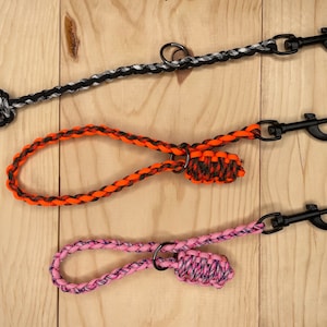 May include: Three different dog leashes with a knotted rope handle and a black metal clip. The leashes are black and white, orange and black, and pink and purple.