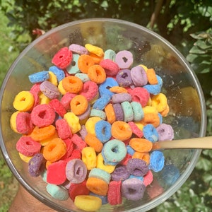May include: A glass bowl filled with colorful cereal rings. The cereal is a mix of red, orange, yellow, green, blue, and purple.