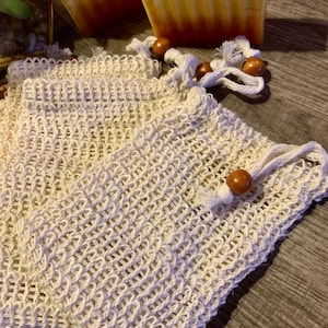 May include: Two white mesh bags with wooden toggles. The bags are made of a fine, woven material and are ideal for holding small items.