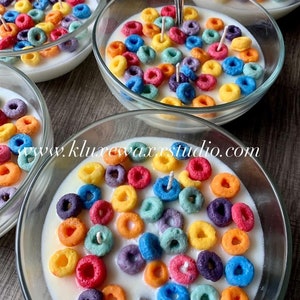 May include: A set of colorful cereal ring candles in glass bowls. The candles are arranged in a bowl with white wax and resemble a bowl of cereal. The candles are a variety of colors, including red, orange, yellow, green, blue, and purple.