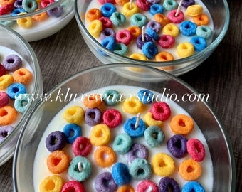 May include: A set of colorful cereal ring candles in glass bowls. The candles are arranged in a bowl with white wax and resemble a bowl of cereal. The candles are a variety of colors, including red, orange, yellow, green, blue, and purple.