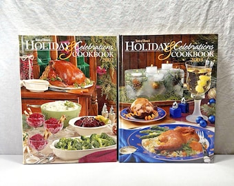 May include: Two cookbooks titled "Holiday Celebrations Cookbook" from 2002 and 2003. The covers feature festive holiday food spreads, including a roasted turkey, side dishes, and a glass of wine. The books are on a white surface.