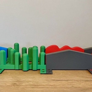 Puede incluir: Un conjunto de rampas impresas en 3D de colores vivos y un obstáculo verde parecido a un arbusto. Las rampas son de plástico azul, gris y rojo. Las rampas están conectadas entre sí y están diseñadas para usarse con coches de juguete u otros vehículos pequeños.