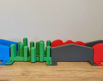 May include: A set of colourful, 3D printed ramps and a green bush-like obstacle. The ramps are made of blue, grey, and red plastic. The ramps are connected to each other and are designed for use with toy cars or other small vehicles.