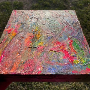 Pu&ograve; includere: Dipinto astratto su tela con una superficie strutturata. Il dipinto presenta una miscela di colori, tra cui rosso, giallo, blu, verde e argento. I colori sono mescolati insieme in un motivo vorticoso, creando una composizione dinamica ed energica.