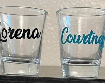Może przedstawiać: Cztery przezroczyste szklanki do shotów z personalizowanymi imionami: Ashley, Lorena, Courtney i Katie. Imiona są napisane kursywą i w różnych kolorach.