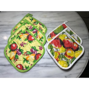 May include: A set of quilted pot holders with fruit designs. One set features red apples, yellow lemons, and green leaves on a white background. The other set has red apples, purple plums, and yellow lemons on a yellow background.