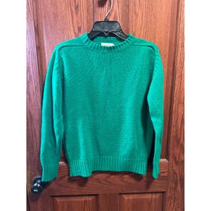 May include: A bright green sweater with a crew neck and long sleeves. The sweater is made of a knitted material and hangs on a black hanger. The sweater has ribbed cuffs and a ribbed hem. The shoulders have a subtle seam detail.