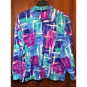 May include: A colorful jacket with a vibrant abstract pattern. The jacket features a collared neckline, long sleeves, and a cinched waist. The design incorporates shades of blue, purple, teal, and white, creating a bold and artistic look. The jacket is made of a lightweight material.