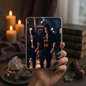 May include: A clear phone case displaying a digital image of three figures in black hooded jackets and skull masks. The image is held by a hand with black nail polish, with candles and books in the background.