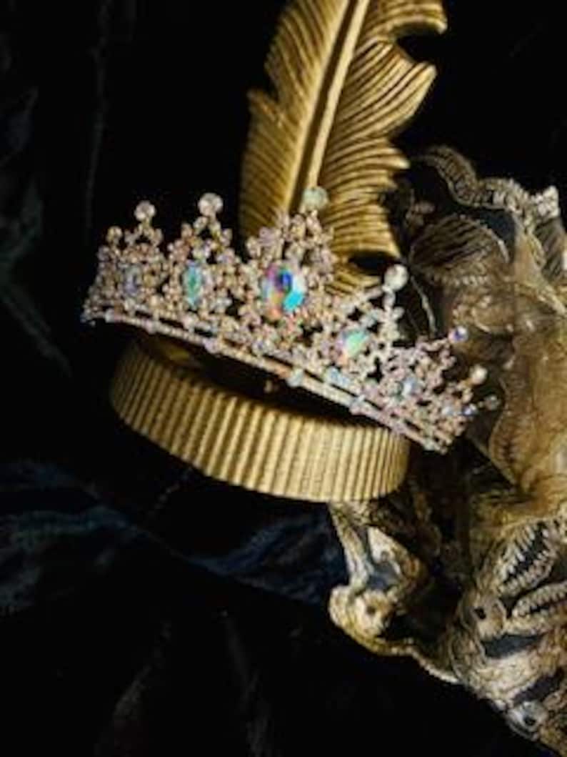Op de afbeelding: Een gouden kroon met heldere, iriserende stenen en een rij kleinere stenen. De kroon staat op een gouden standaard.