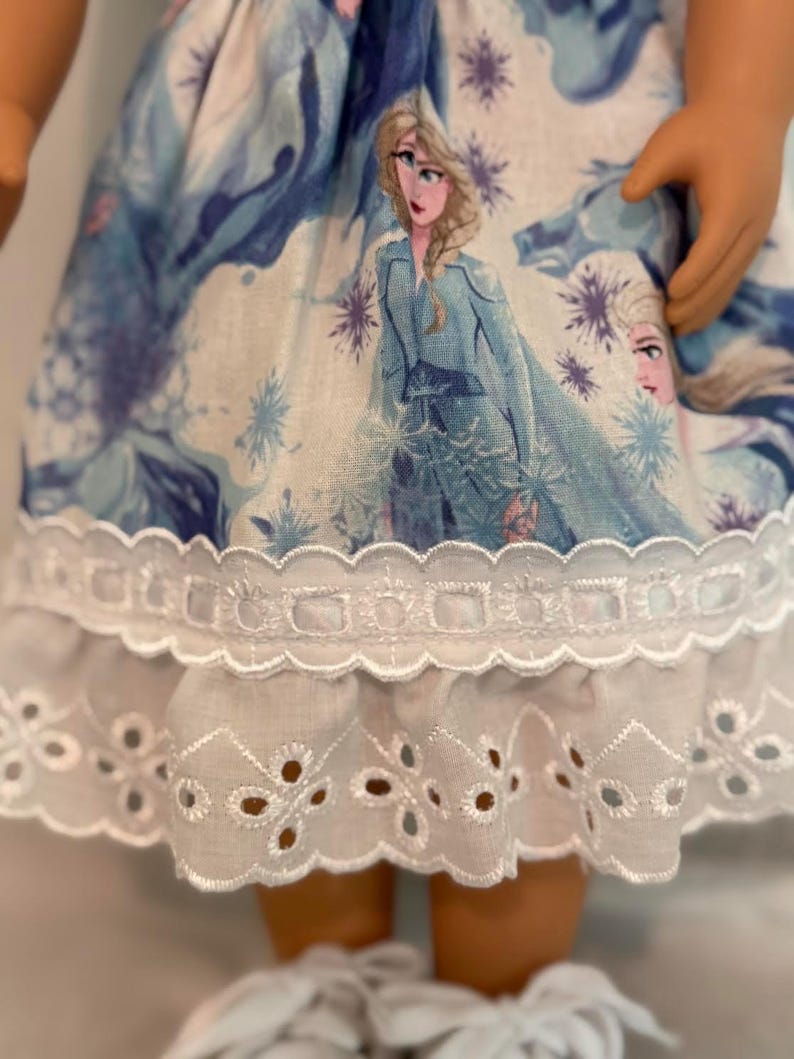 Puede incluir: Una mu&ntilde;eca con un vestido azul claro y blanco con un dise&ntilde;o de princesa. El vestido tiene un ribete de encaje de ojal blanco en el dobladillo. Se ven los brazos y las piernas de la mu&ntilde;eca.