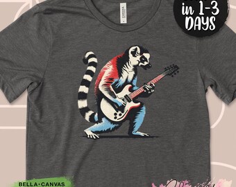 Könnte beinhalten: Dunkelgraues T-Shirt mit einem Lemuren, der E-Gitarre spielt. Der Lemur ist in Rot, Weiß und Blau dargestellt. Das Shirt hat den Text "BELLA+CANVAS USA STRONG AIRLUME COTTON ECO-FRIENDLY" und "SHIPS in 1-3 DAYS".