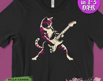 May include: Black t-shirt featuring a cat playing an electric guitar. The cat is depicted in shades of purple and cream. The shirt has the text "BELLA + CANVAS USA STRONG AIRLUME COTTON ECO-FRIENDLY" and "SHIPS in 1-3 DAYS".