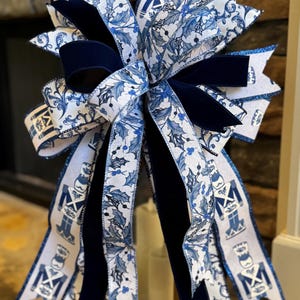 May include: A large decorative bow featuring a combination of blue and white ribbons. The bow has a central velvet section in a deep navy blue. Some ribbons display a holly and berry pattern, while others feature a toy soldier design. The edges are trimmed with glitter.