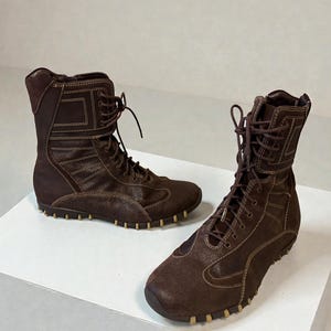 May include: A pair of brown suede and leather boots with a lace-up design. The boots have a high-top style with a padded collar and a rubber sole. The boots are approximately 8 inches tall.