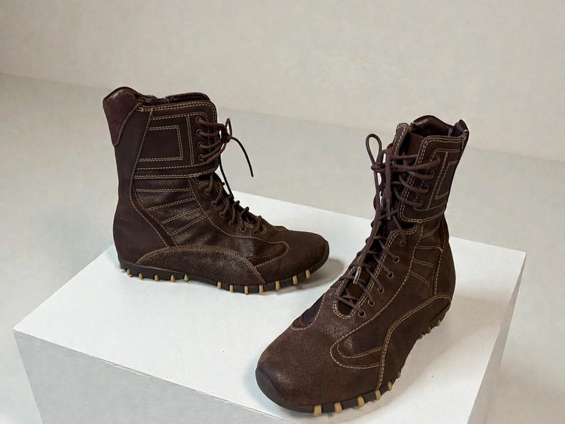 May include: A pair of brown suede and leather boots with a lace-up design. The boots have a high-top style with a padded collar and a rubber sole. The boots are approximately 8 inches tall.