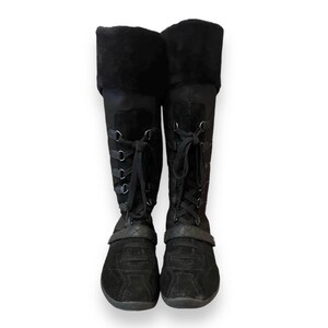 May include: Black suede knee-high boots with lace-up detailing and a black strap across the top of the foot.