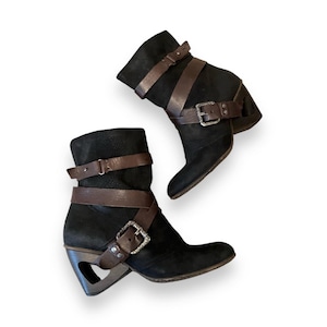 May include: A pair of black leather ankle boots with brown leather straps and buckles. The boots have a chunky heel and a unique cut-out design on the side.
